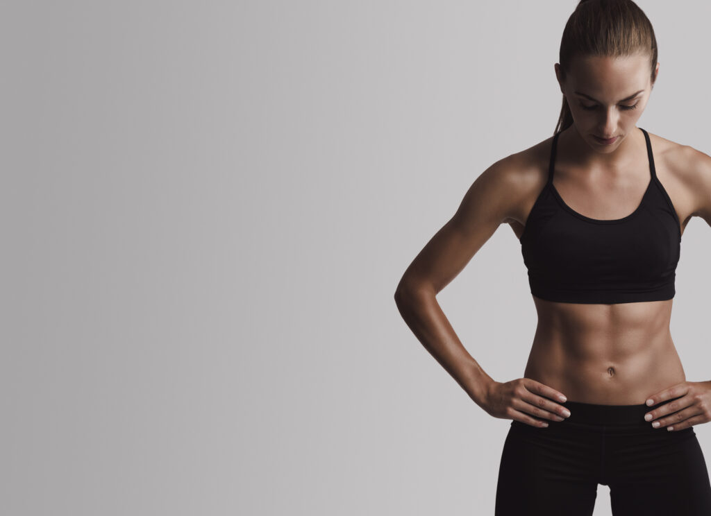 Trenująca kobieta stoi w czarnym stroju treningowym, posiada bardzo umięśniony brzuch.